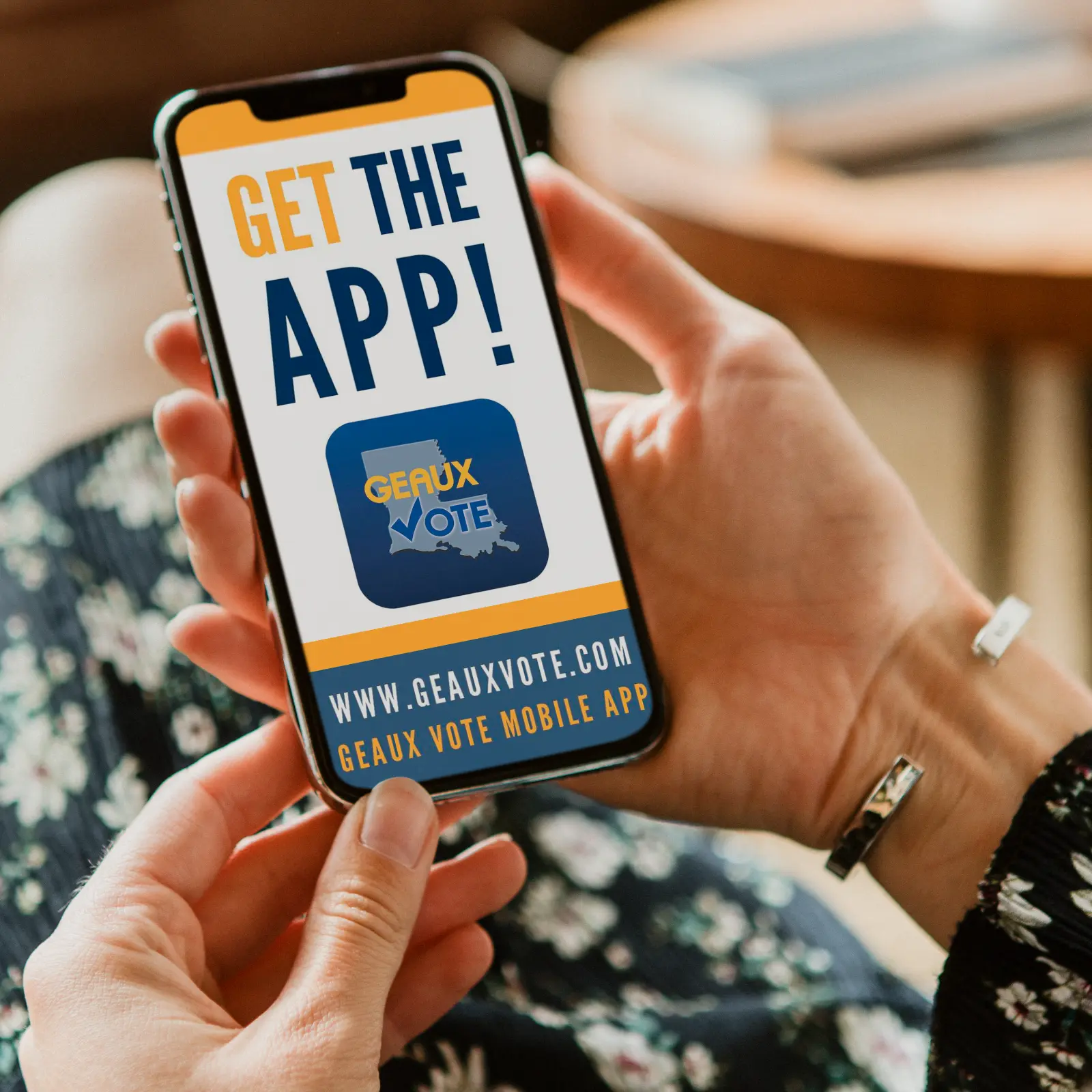 Person holding a smartphone displaying a message to get the Geaux Vote mobile app at www.geauxvote.com.