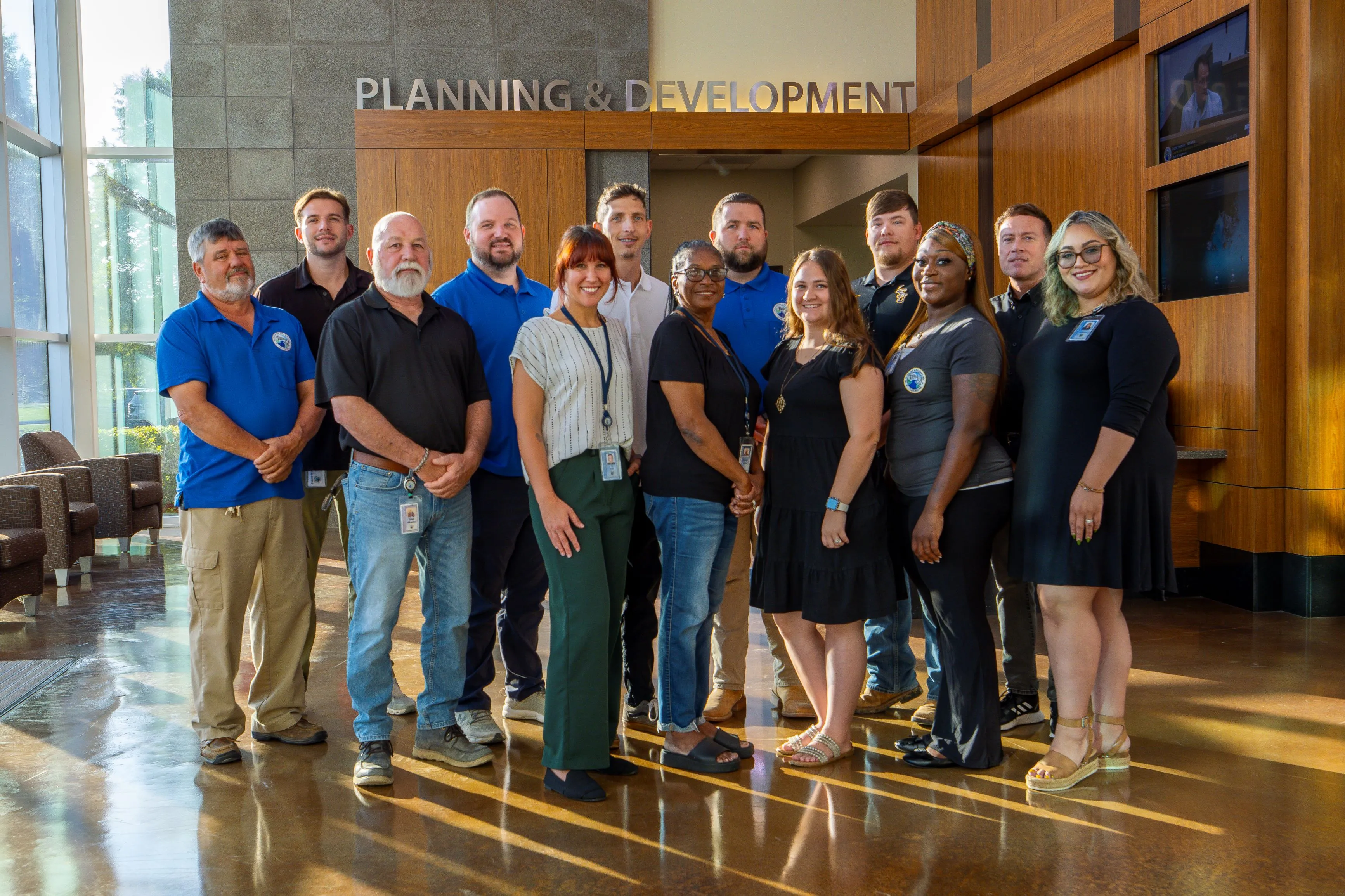 Group of diverse people standing in a lobby under a sign reading 'Planning & Development', smiling and posing for a photo.