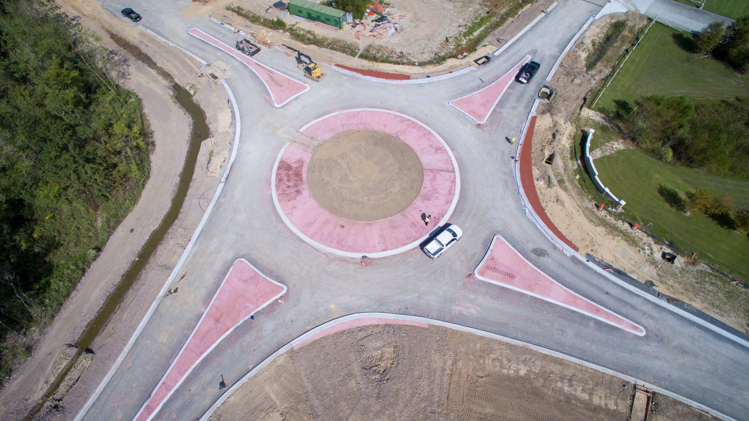 Aerial view of a construction site featuring a partially completed roundabout with pink concrete islands and surrounding earthwork.