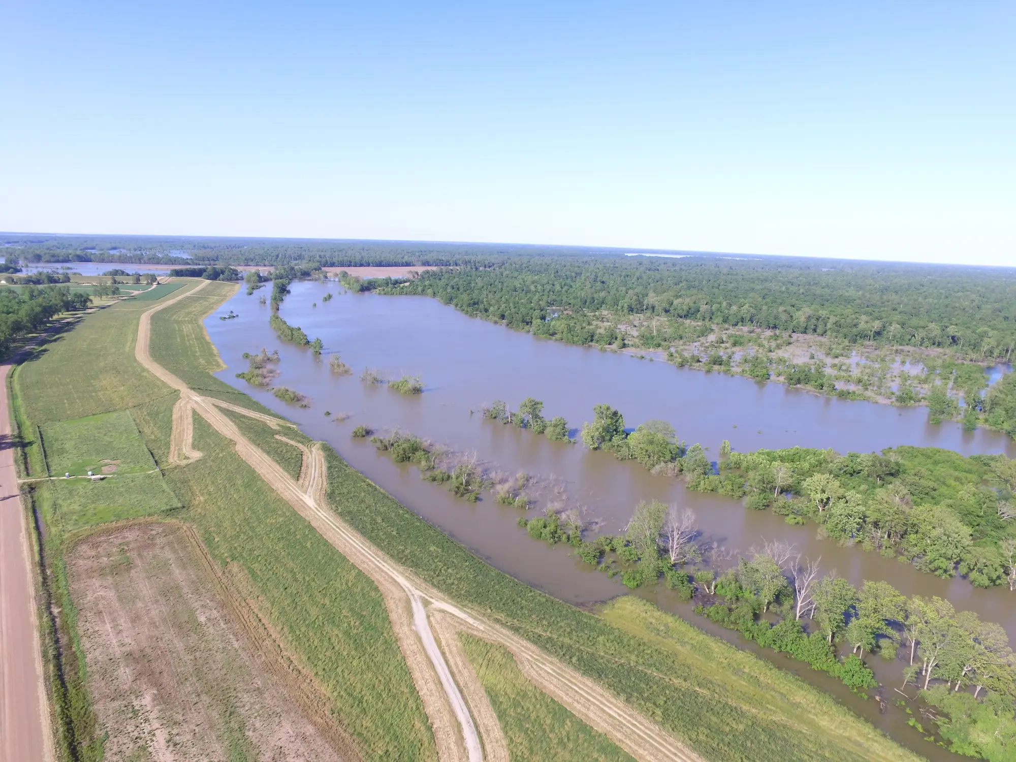 Aerial view of a river with surrounding farmland and forest under a clear blue sky.