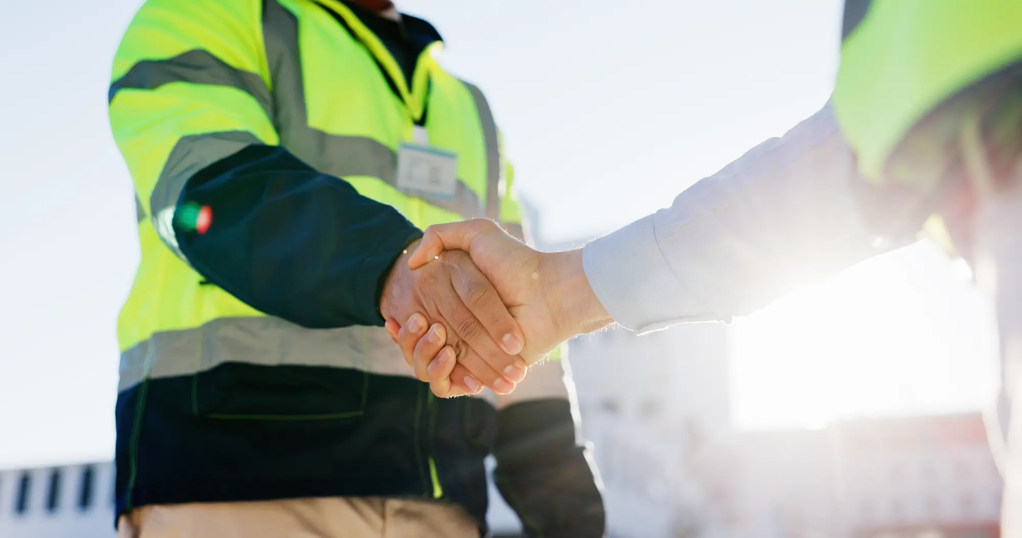 Two people shaking hands, one wearing a high-visibility safety jacket.