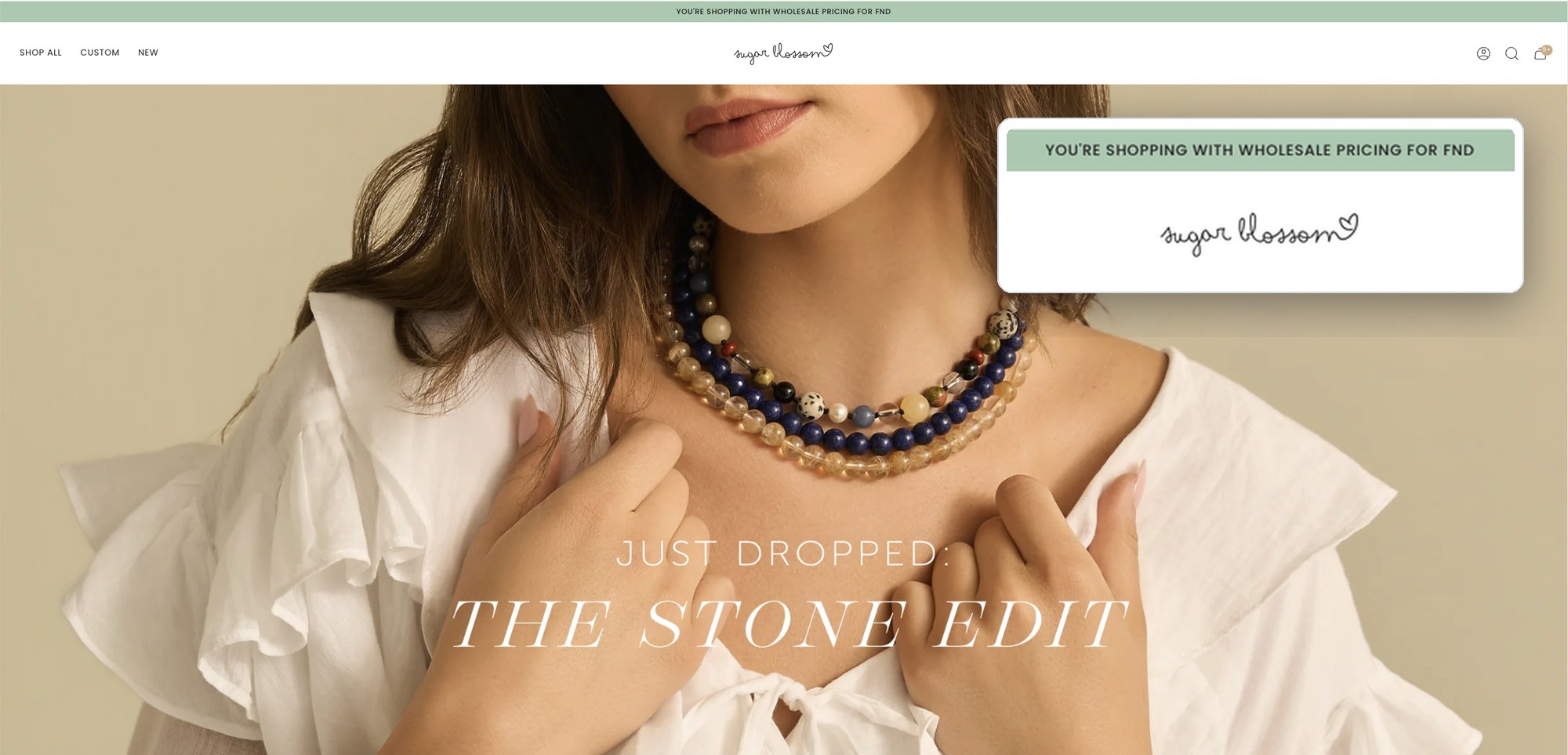 Sugar Blossom homepage logged in as a wholesale buyer. A green bar above the header reads You're shopping with wholesale pricing for FND, shown enlarged in a callout, above the Stone Edit campaign photo.