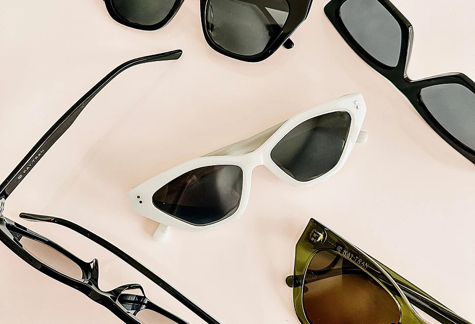 Several pairs of sunglasses from Kaytran Eyewear, including a standout white pair, are arranged on a light-colored surface, bringing a touch of Winnipeg style with various frame shapes and colors.