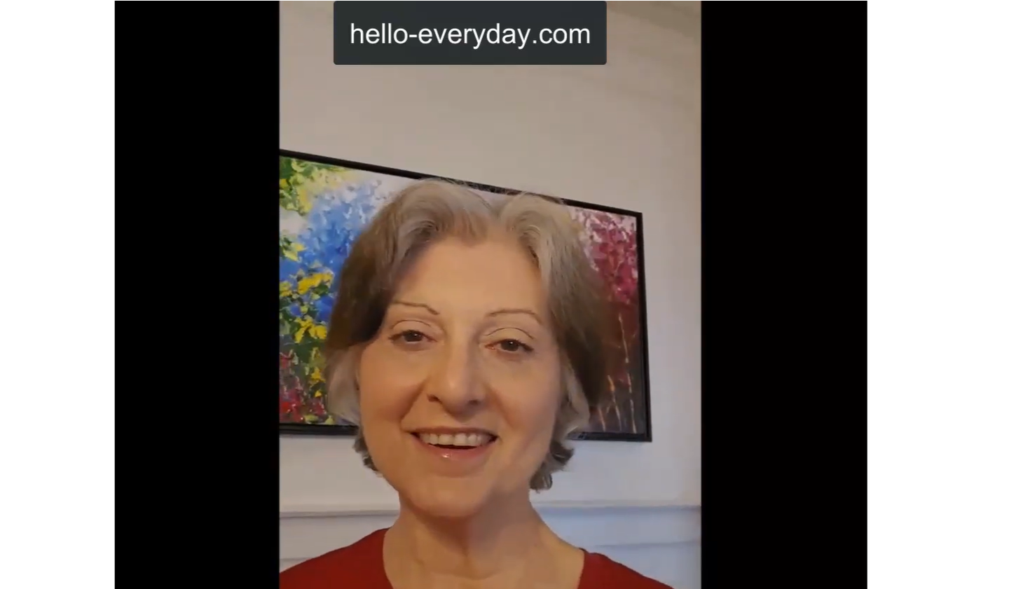 Smiling middle-aged woman with short gray hair wearing a red top in front of a colorful floral painting.