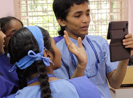 A teacher holding a tablet while students gather around her