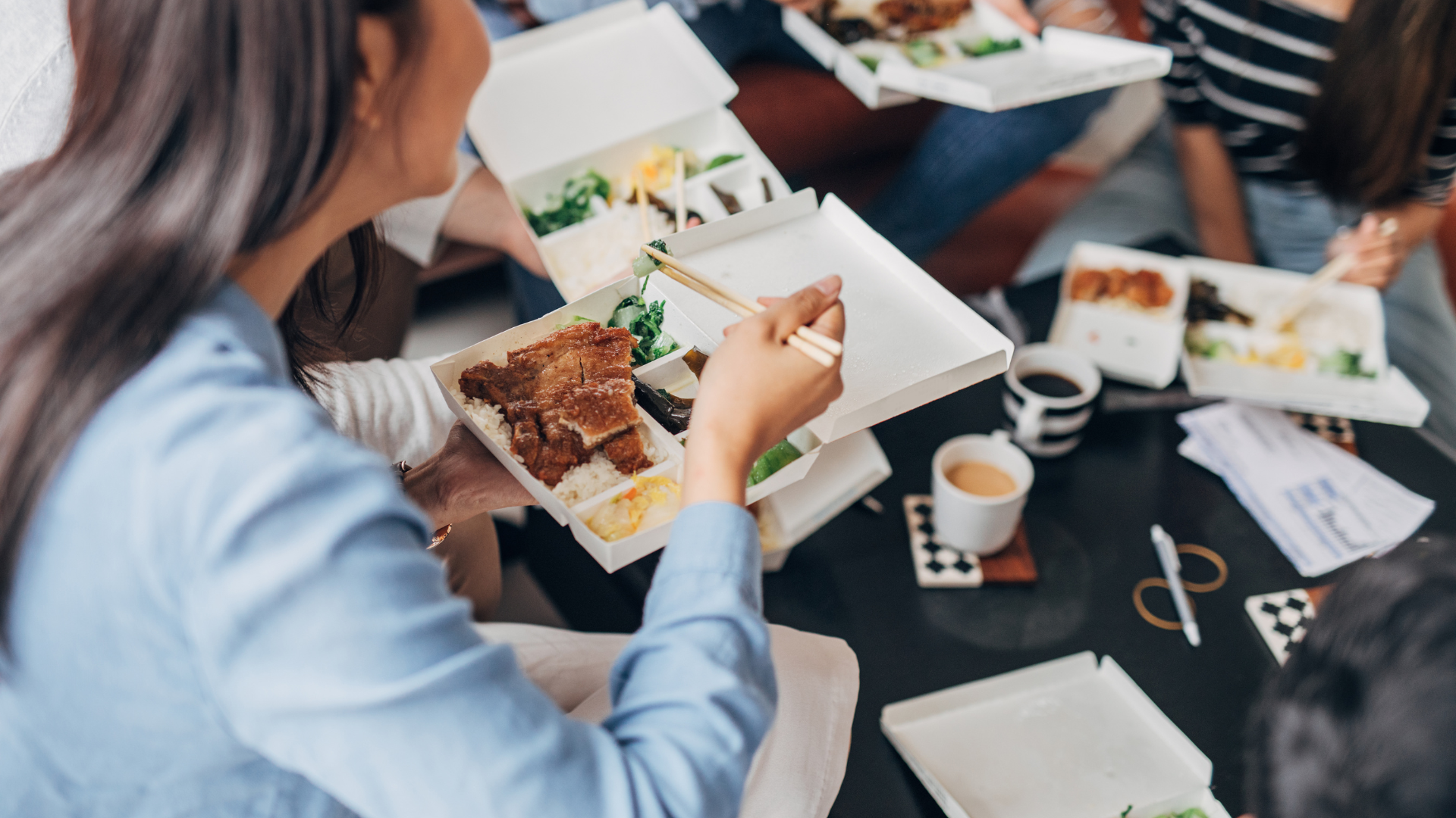 Group of coworkers eating lunch from takeaway bento boxes in an office setting