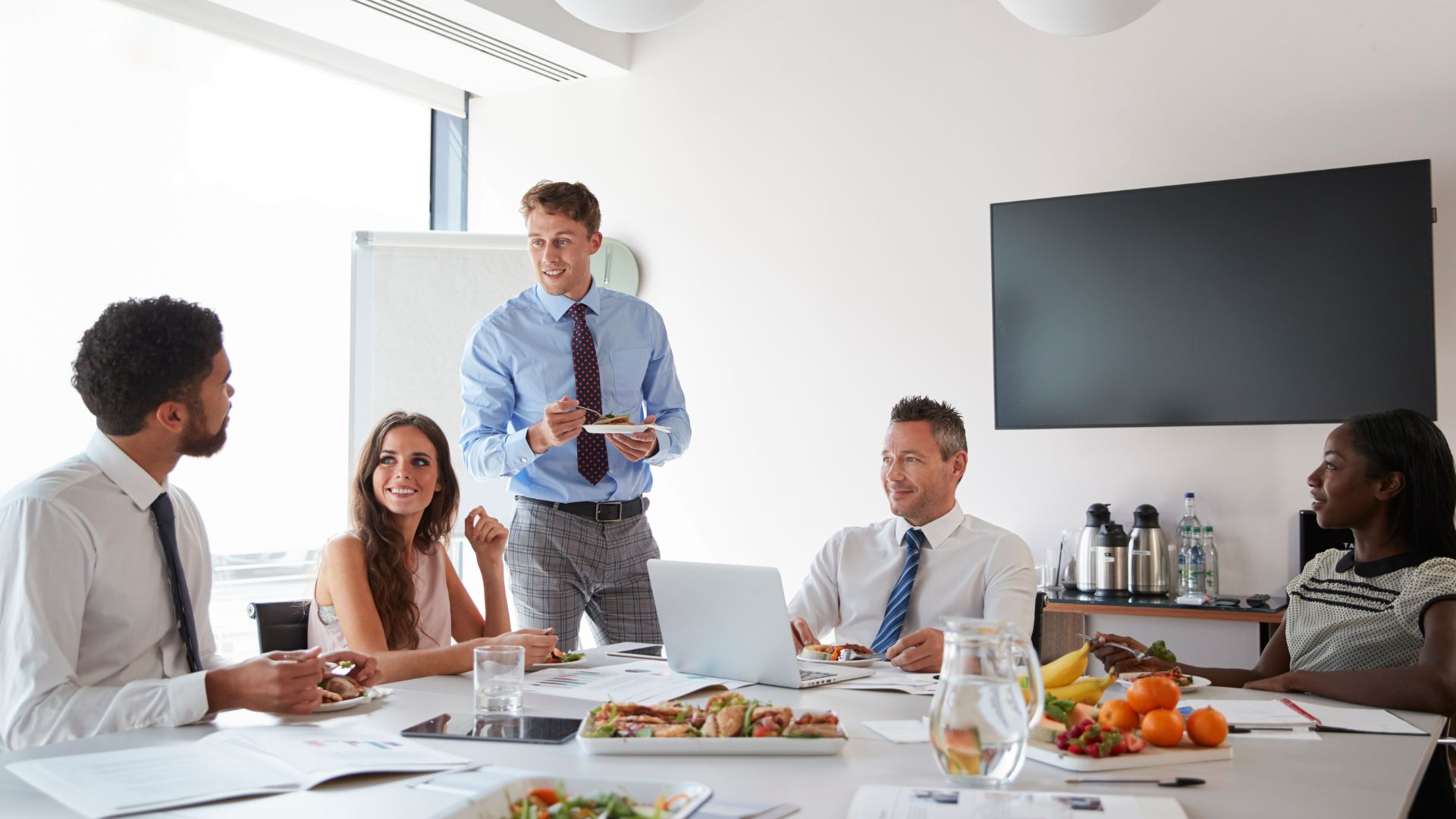 Corporate lunch catering in London – colleagues enjoying catered lunch during a business meeting with healthy platters and fruit on the table.