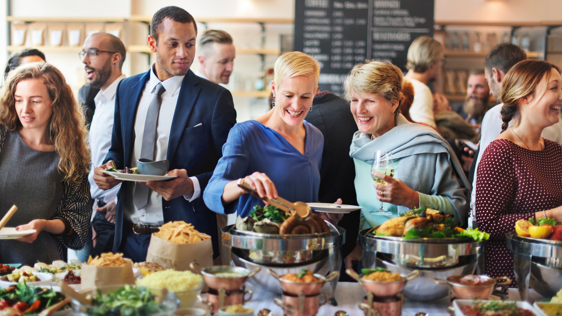 Corporate buffet catering with guests serving themselves from chafing dishes filled with salads, hot food, and appetizers at a business event