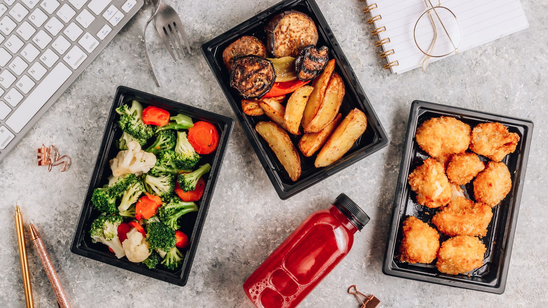Healthy office lunch catering with roasted vegetables, broccoli, chicken bites, and fresh juice at the workplace desk