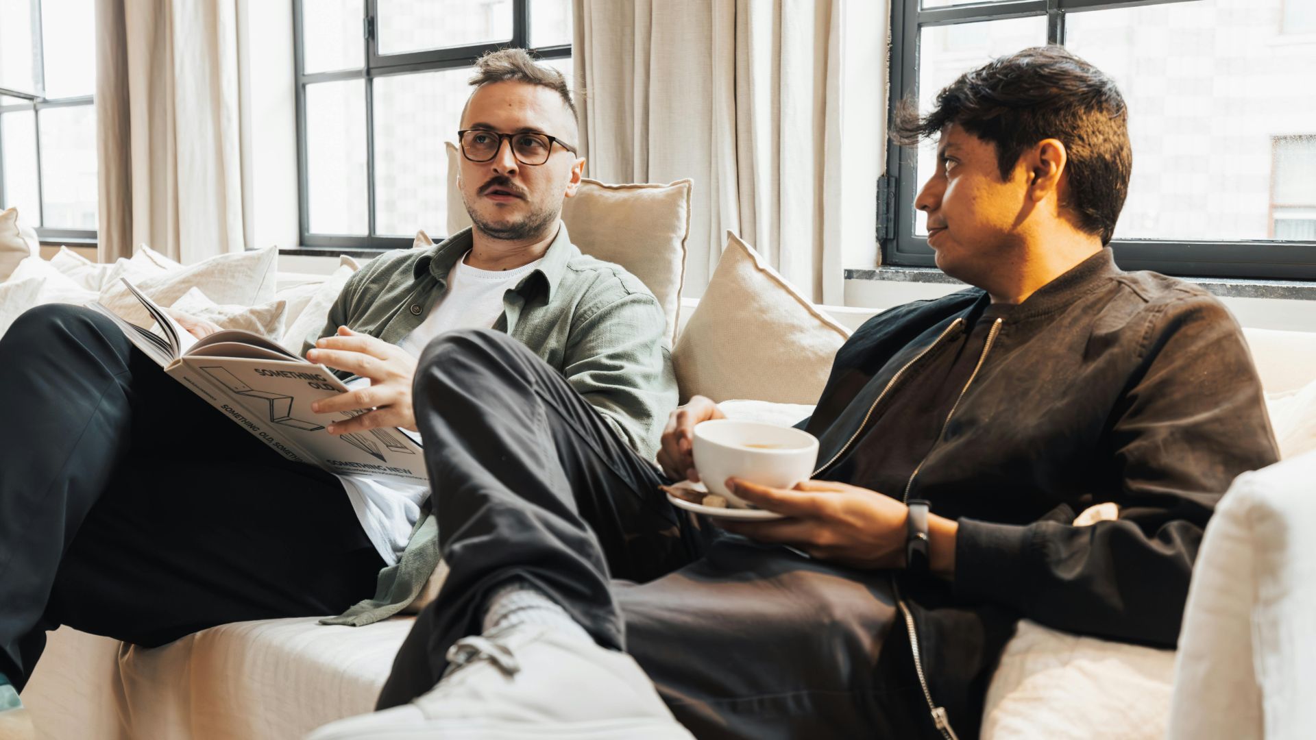 Two colleagues relaxing on an office sofa discussing ideas over coffee during an informal meeting.