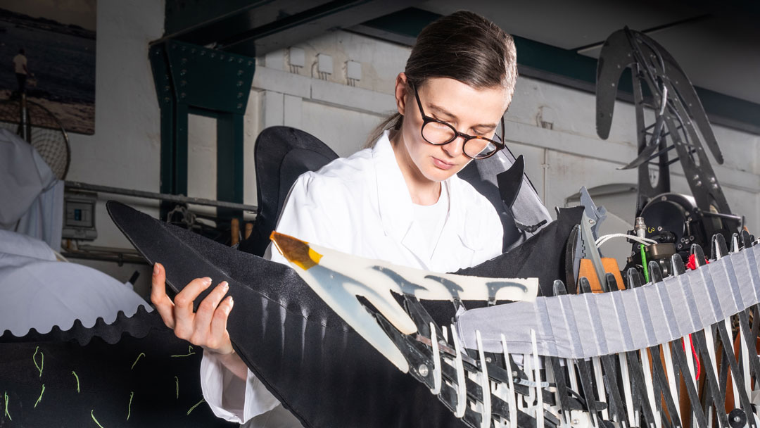 Scientist with glasses and white lab coat examining a complex mechanical device with metal and fabric components.