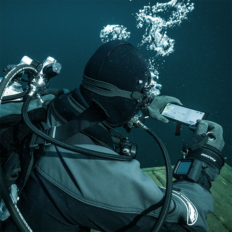 Scuba diver underwater wearing full gear and looking at a smartphone displaying a navigation map.