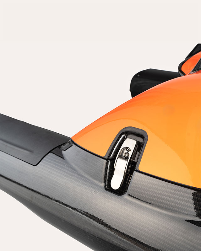 Close-up of a black carbon fiber and orange component with a shiny metal latch.