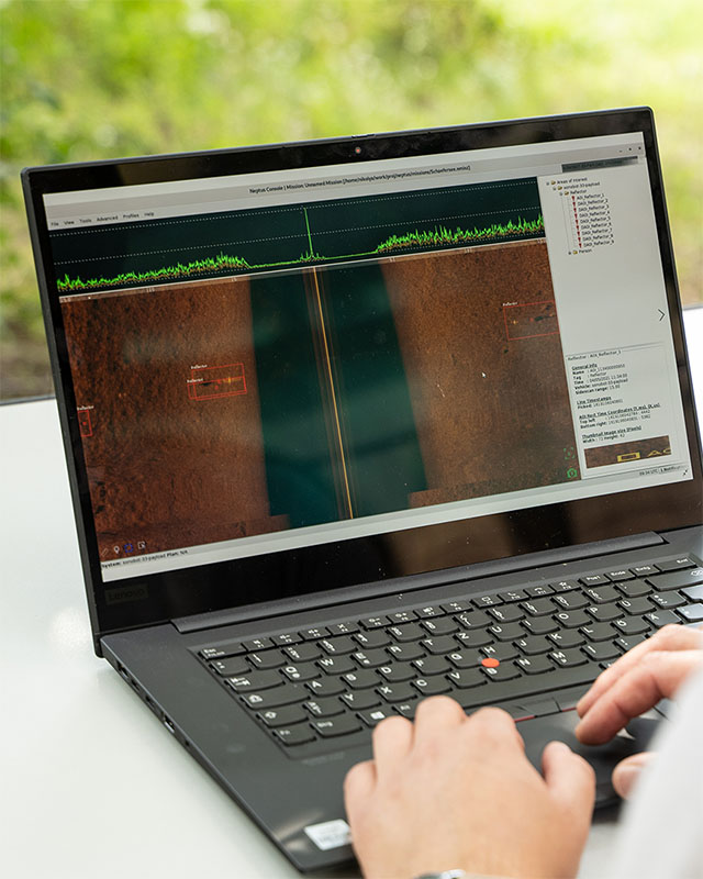 Person using a Lenovo laptop displaying sonar scan data with highlighted sections and a green signal graph.