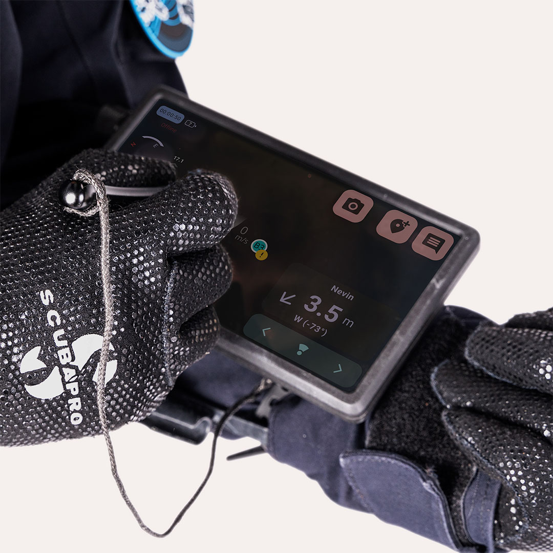 Gloved hands operating a Scubapro dive computer showing 3.5 meters depth and navigation info.