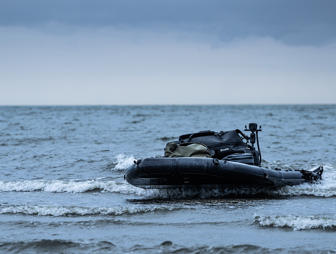 Black inflatable boat with packed bags floating on calm sea under cloudy sky.