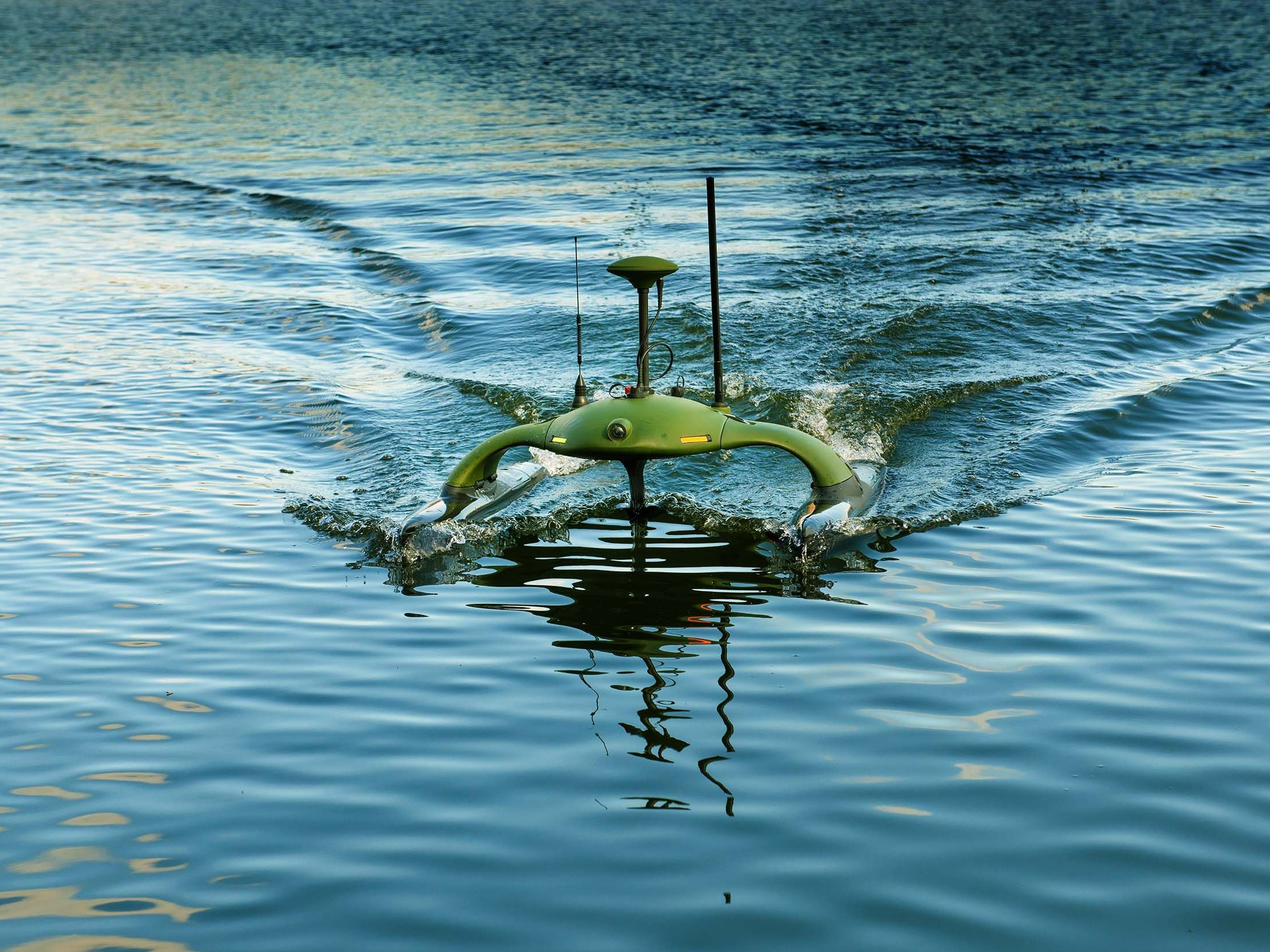 Green autonomous water drone creating ripples as it moves across calm water.