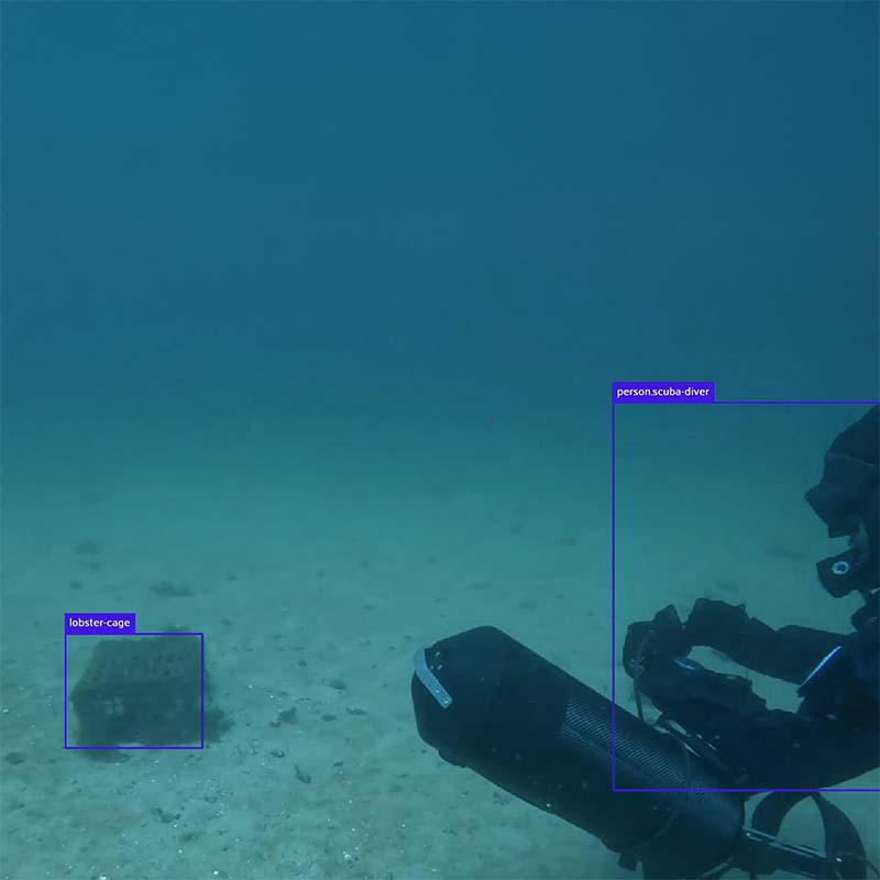 Underwater view of a scuba diver examining a lobster cage on a sandy ocean floor.