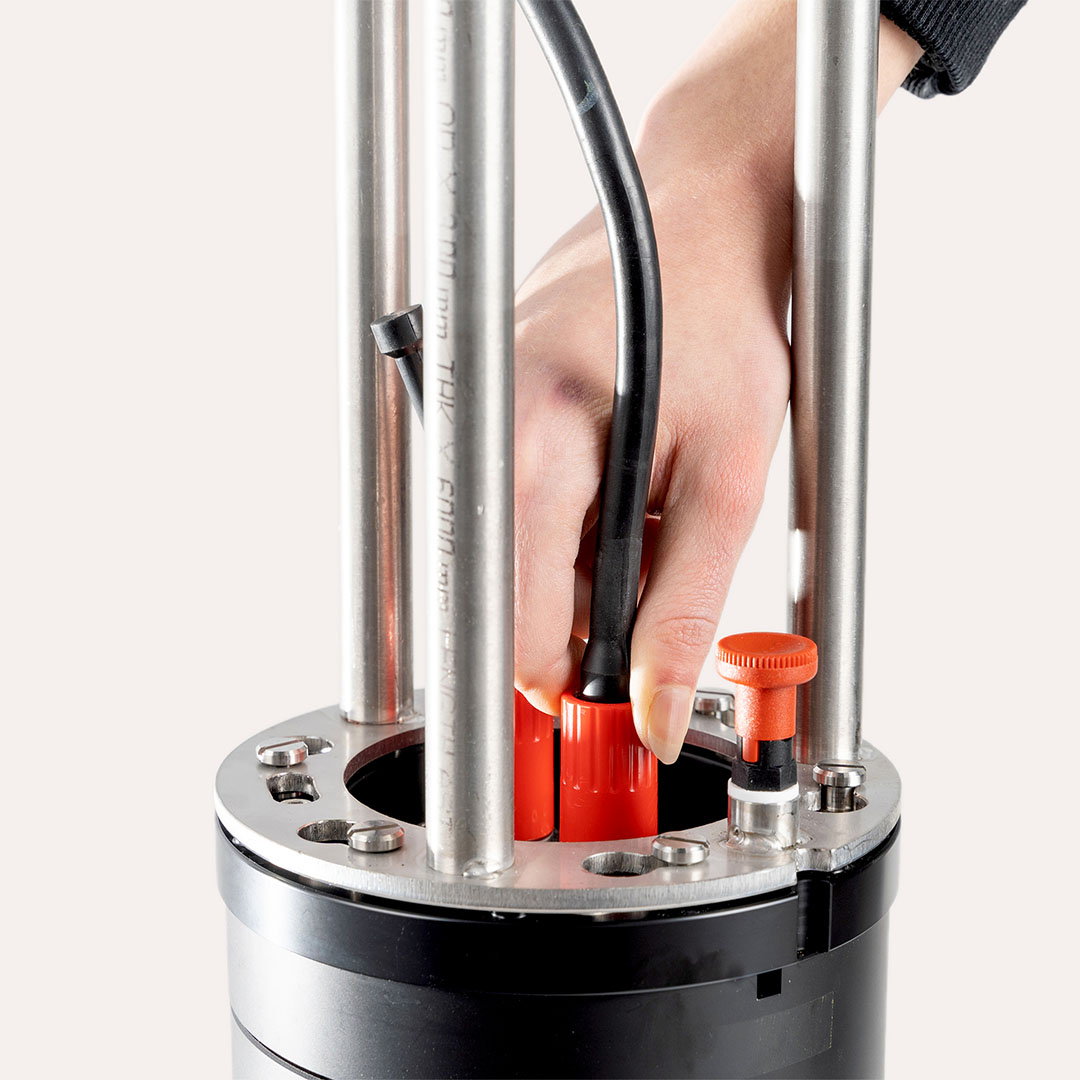 Hand connecting a black cable to a red terminal on a metallic cylindrical device with vertical rods.