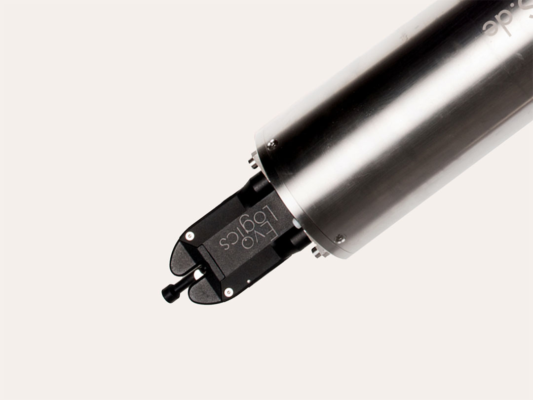 Close-up of a metallic robotic arm end-effector with black gripper labeled EVO Logics against a light background.