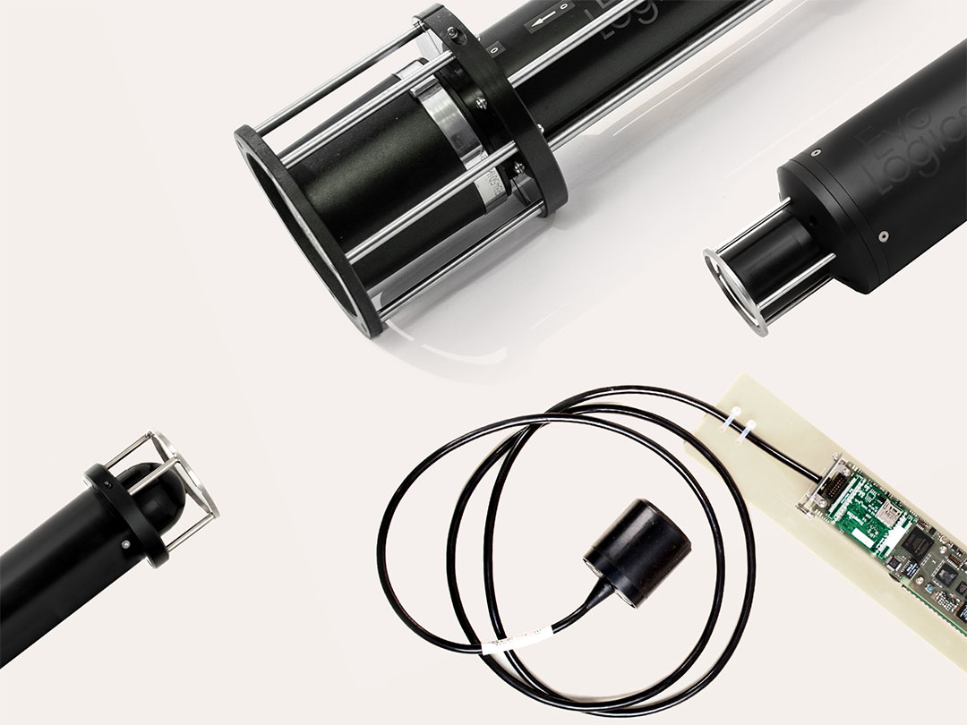 Black cylindrical mechanical devices with metal rods and a connected electronic circuit board with a coiled black cable on a light background.