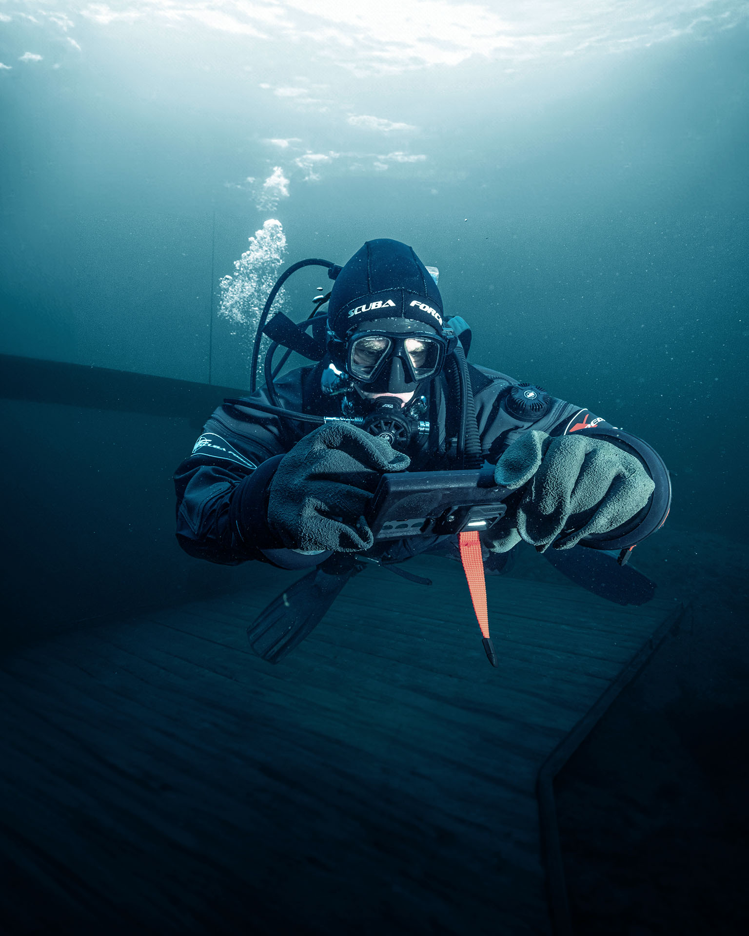 Scuba diver underwater holding a handheld device while wearing full diving gear and gloves.