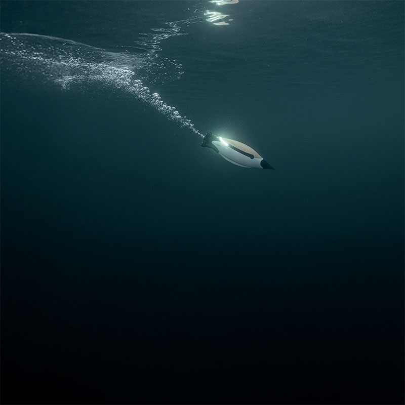 Underwater view of a white and black underwater scooter emitting bubbles as it moves.