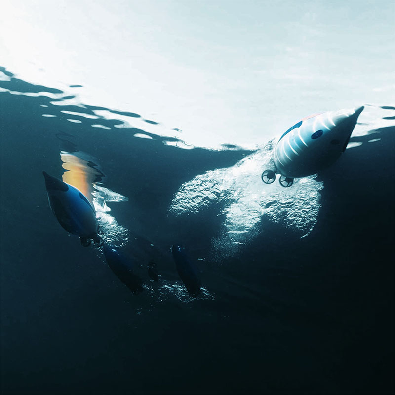 Underwater view of several torpedo-shaped underwater drones moving through dark water towards the surface.