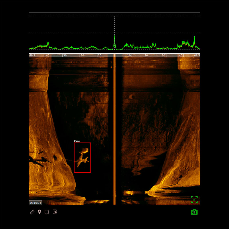 Sonar image showing underwater rock formations with a small airplane detected and highlighted in a red box.