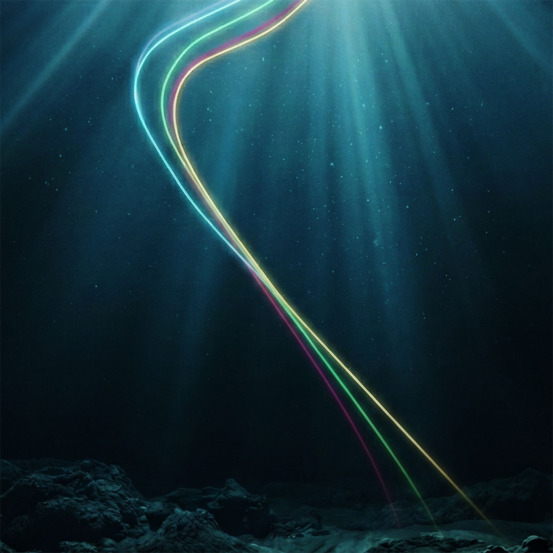 Underwater scene with three colorful light trails curving upward through dark water above rocky seabed.