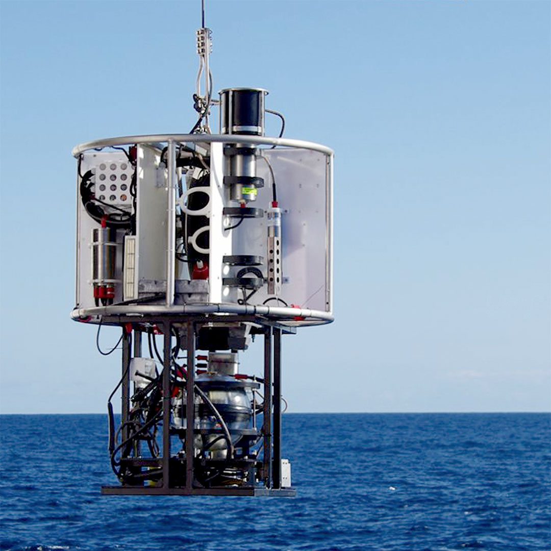 Scientific oceanographic instrument suspended above the sea surface with a clear sky background.