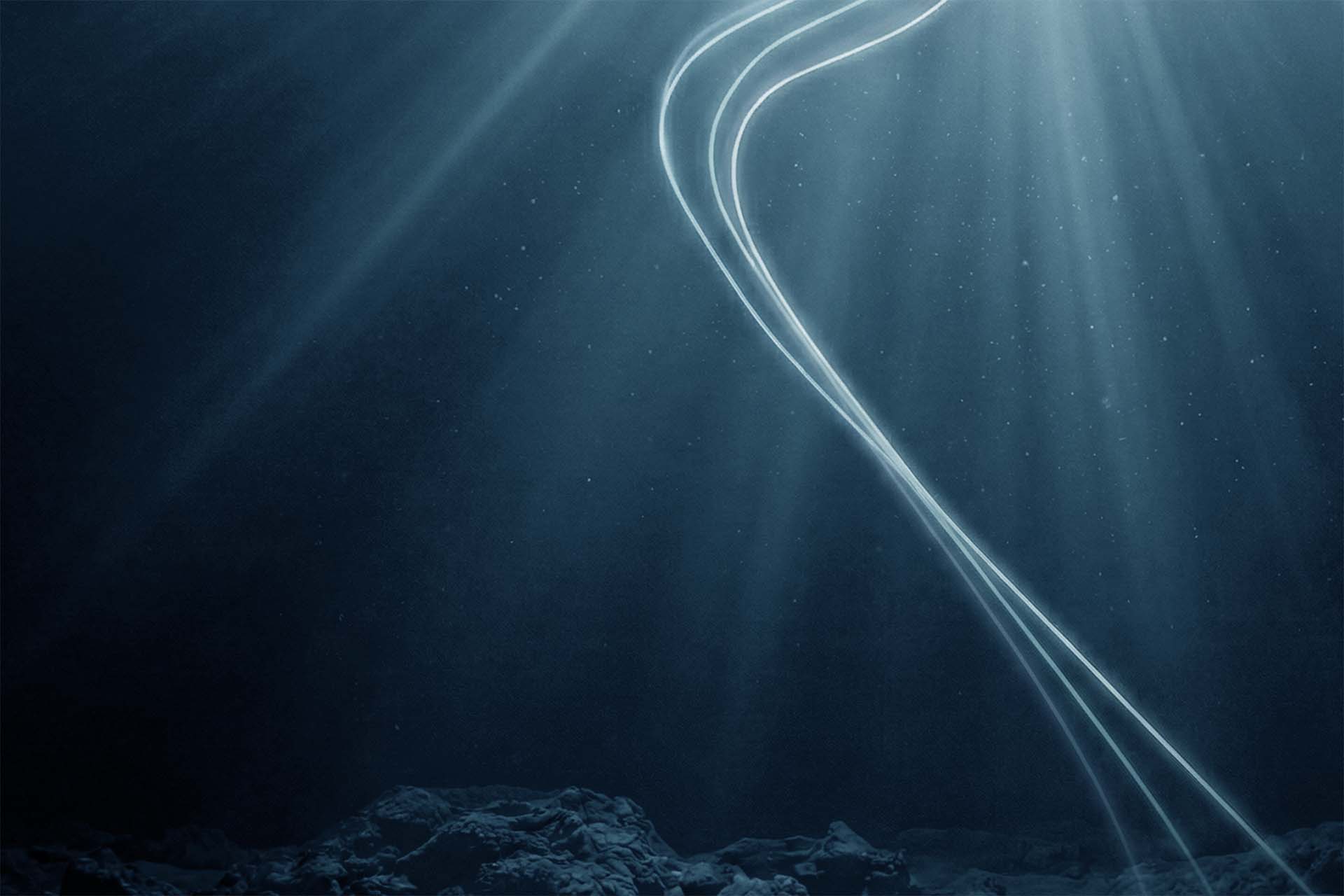 Underwater scene with rocky seabed and beams of light shining through water, illuminating flowing light trails.