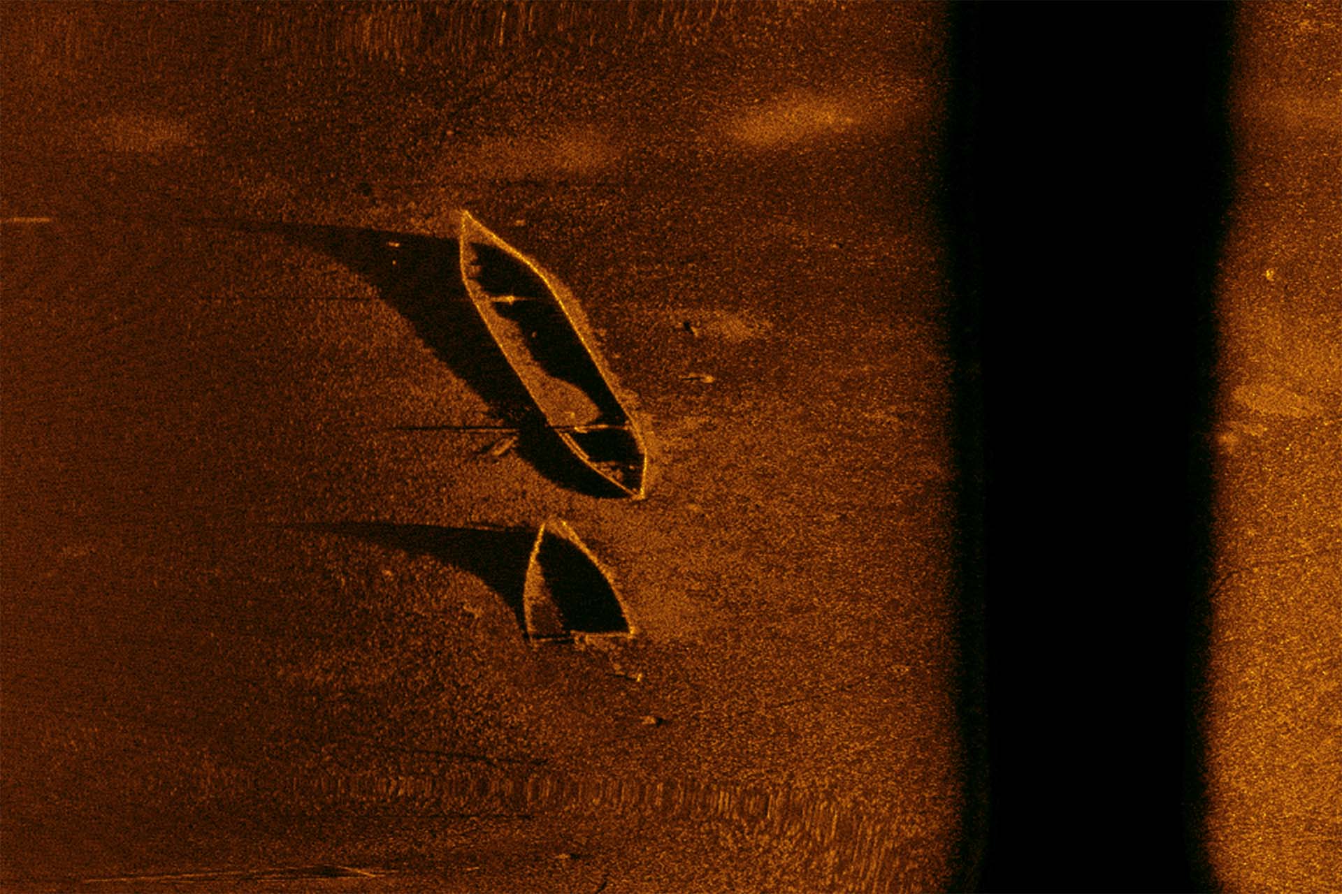 Sonar image showing two submerged boats lying on the seafloor with their shadows cast beneath them.
