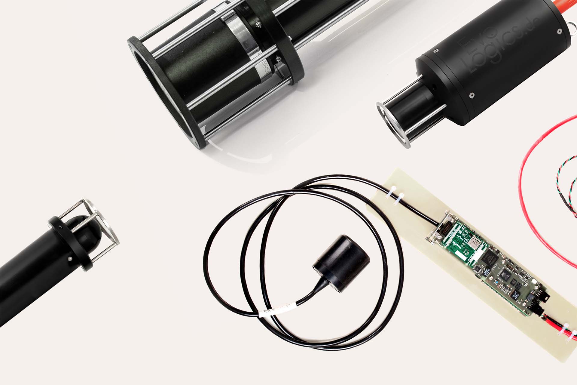 Four black cylindrical electronic components with metal supports and a circuit board on a light background.