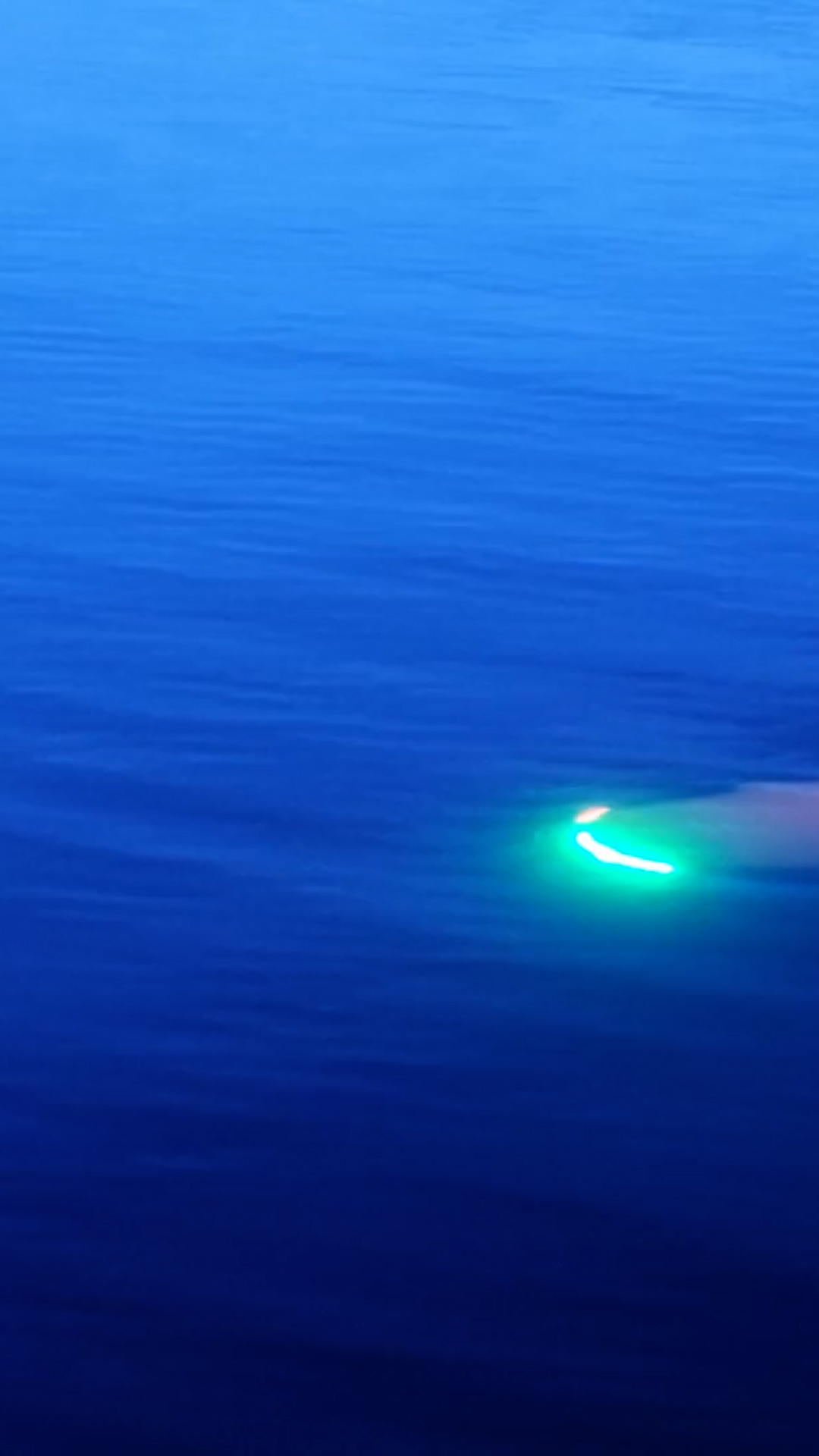 Blue ocean water at dusk with a boat's green navigation light glowing on the right side.