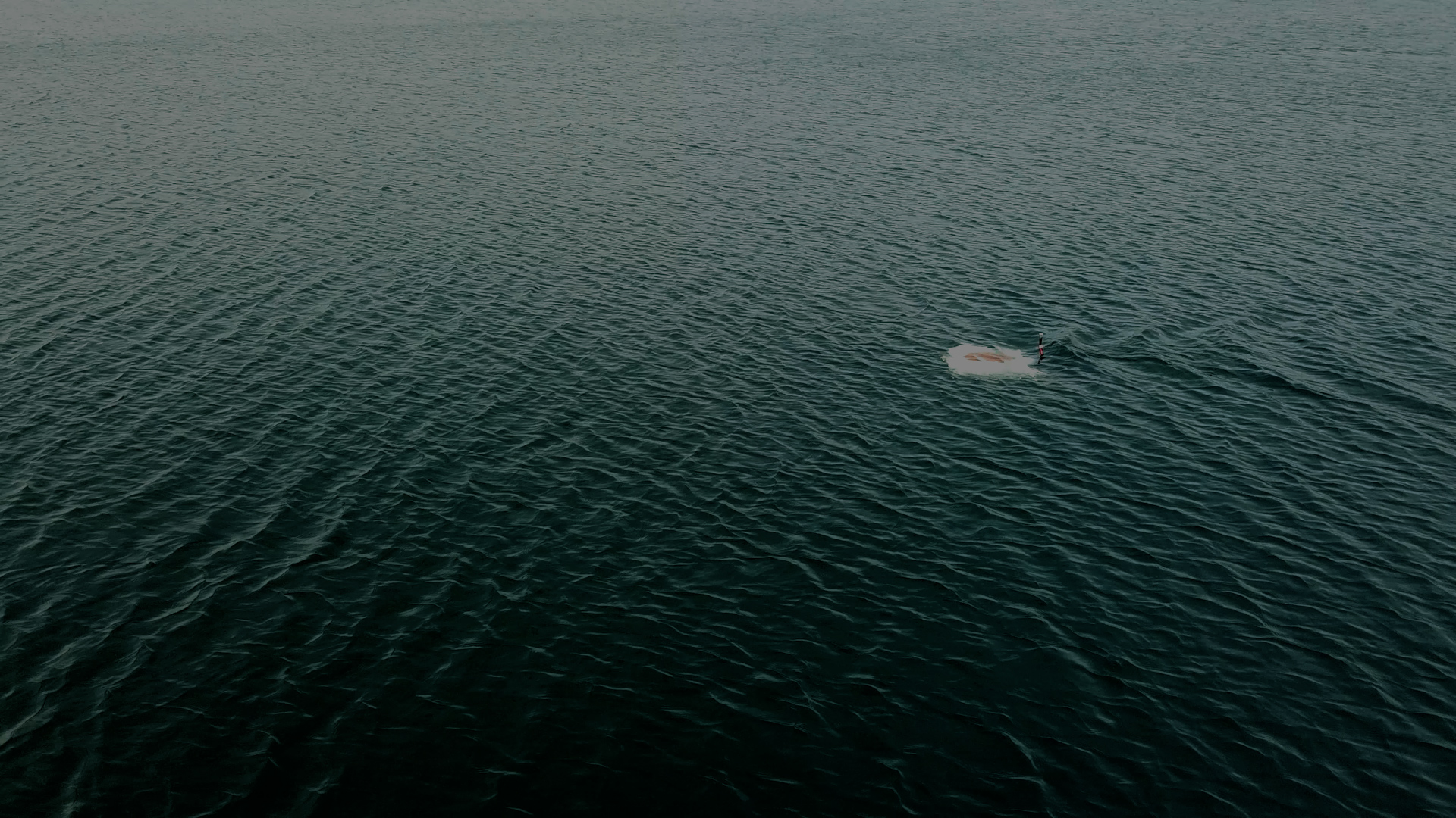 Person wakeboarding on dark rippled water leaving a trail behind.
