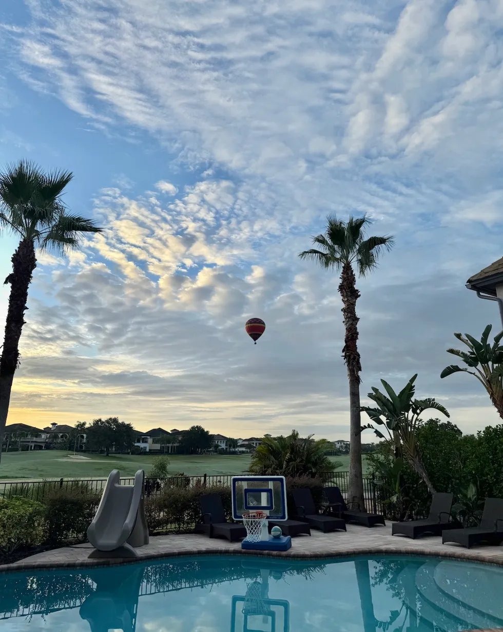 Hot air balloon floating over the Jack Nicklaus golf course at sunrise, viewed from The Luxe Palmilla private pool deck at Reunion Resort, Orlando Florida