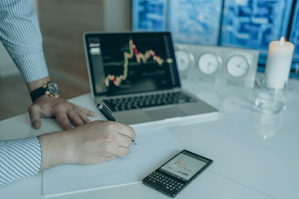 Investisseur analysant des graphiques boursiers sur un ordinateur portable tout en prenant des notes