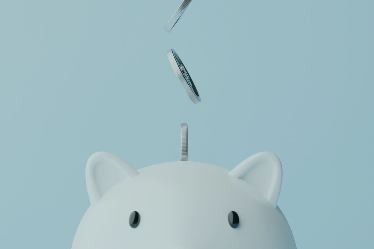 Tirelire blanche avec des pièces qui tombent à l'intérieur, illustrant un plan d'épargne en actions (PEA) qui atteint son plafond de versement.