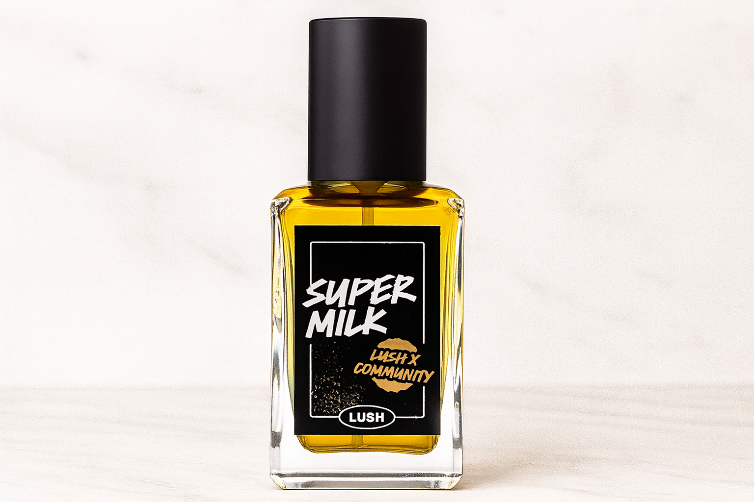  Bottle of Lush Super Milk perfume with a black label and cap, featuring white and gold text, placed on a light marble background.