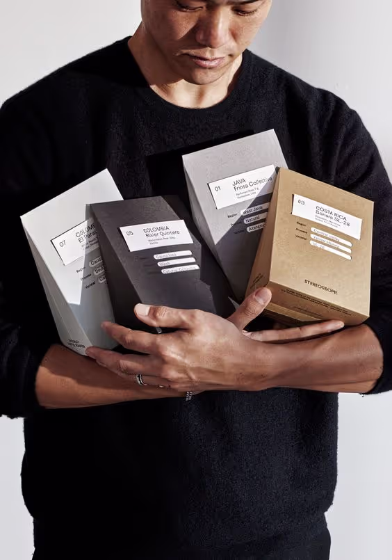 Person wearing a black sweater holding four coffee packaging boxes labeled with different coffee origins.