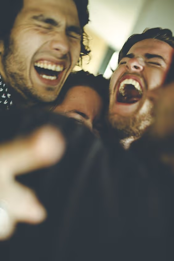 Three friends closely huddled together laughing joyfully with eyes closed.
