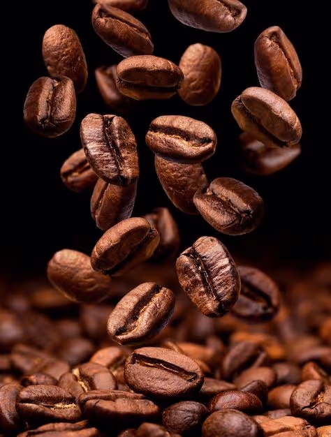 Close-up of medium roasted coffee beans falling above a pile of coffee beans on a black background.