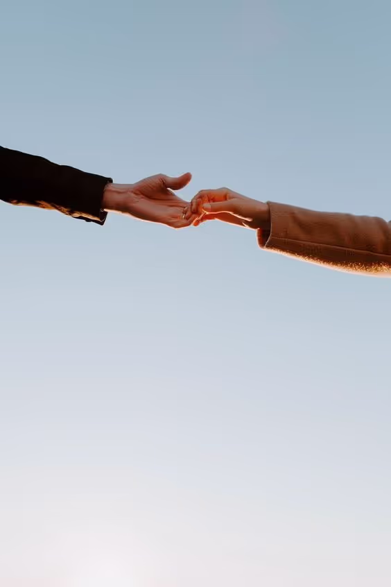 Two hands reaching towards each other against a clear blue sky.
