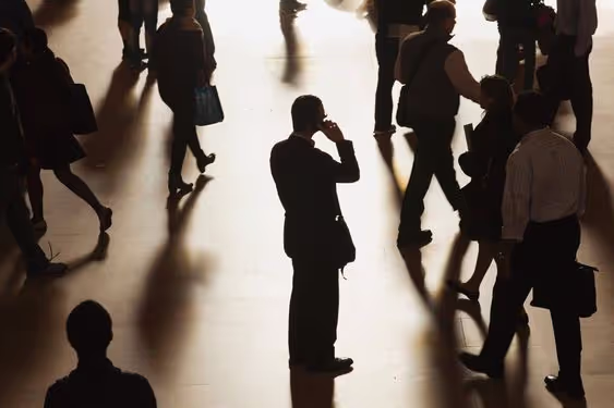 Silhouettes of people walking and standing on a reflective floor, with one person in the center talking on a phone.