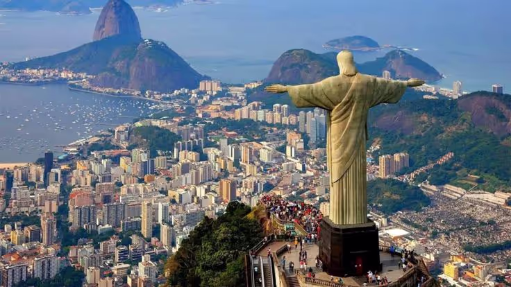 Aerial view of the Christ the Redeemer statue overlooking the city of Rio de Janeiro with Sugarloaf Mountain and Guanabara Bay in the background.