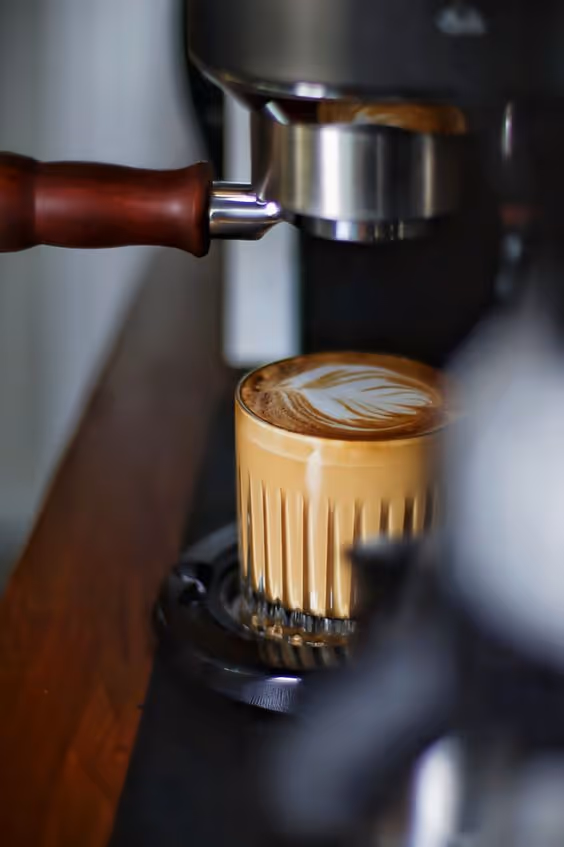 Close-up of a latte with leaf latte art beneath an espresso machine portafilter.