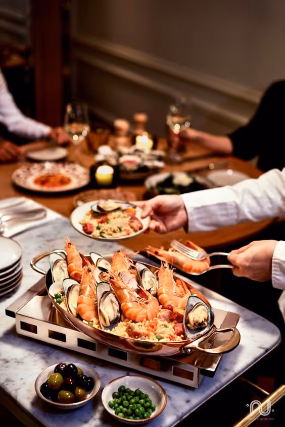 Serving a dish of seafood paella with shrimp and mussels at a dining table set for a meal.