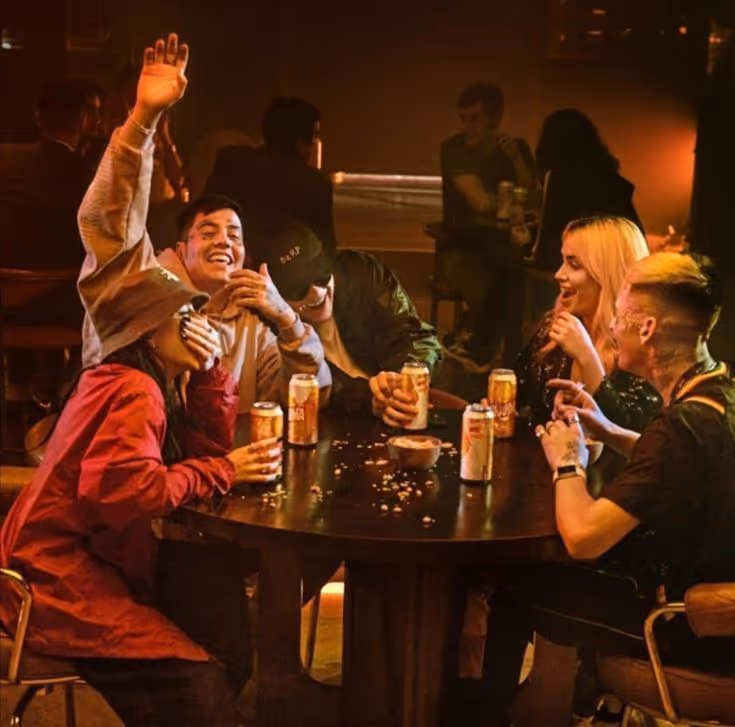 Group of five friends laughing and enjoying drinks around a table in a dimly lit bar.