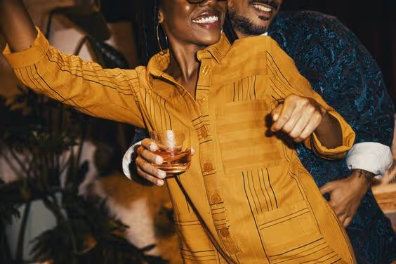 Smiling couple dancing closely, woman in yellow shirt holding a glass.